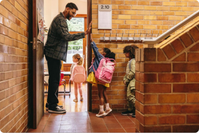 Teacher in hallway, welcoming kids into class . High-fiving one student as she enters with another student behind her.
